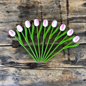 May include: A bouquet of 12 pink and white artificial tulips with green stems arranged in a fan shape on a rustic wooden background.