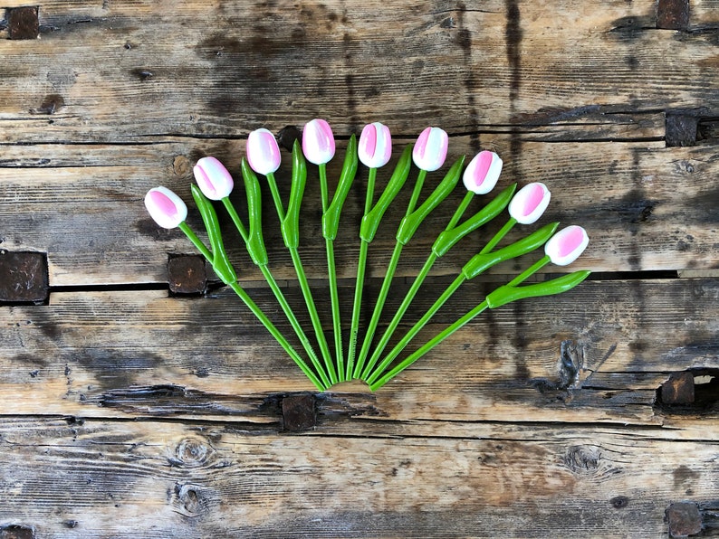 May include: A bouquet of 12 pink and white artificial tulips with green stems arranged in a fan shape on a rustic wooden background.