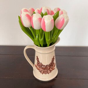 May include: A bouquet of pink and white artificial tulips in a cream-coloured ceramic jug with a brown floral design.