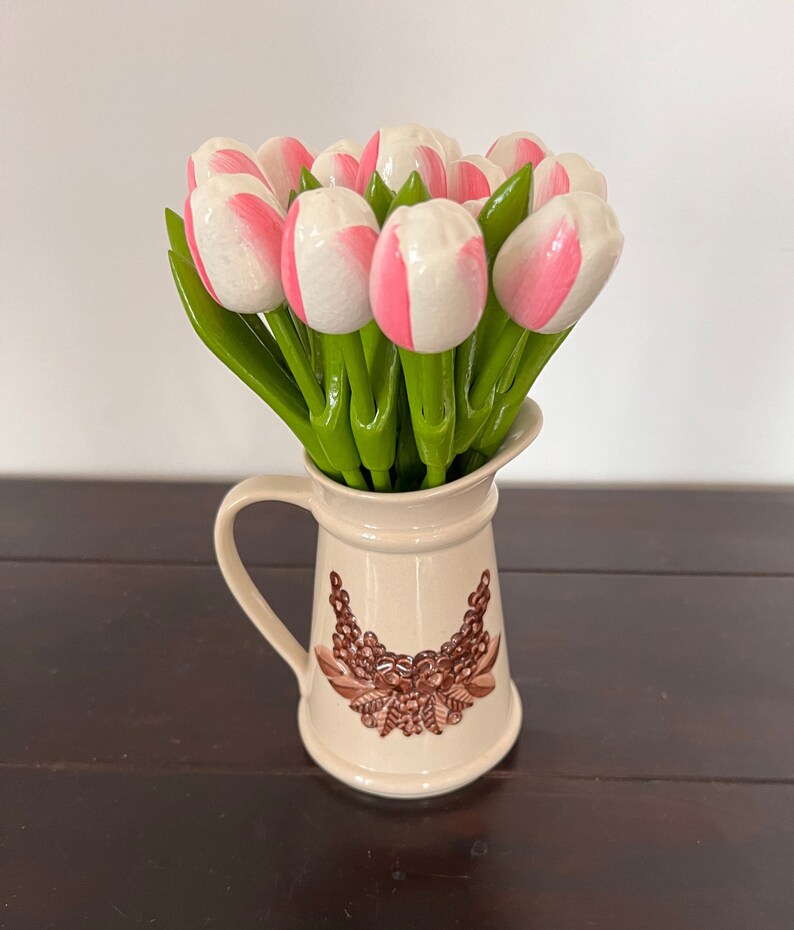 May include: A bouquet of pink and white artificial tulips in a cream-coloured ceramic jug with a brown floral design.