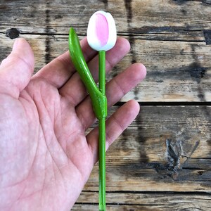 May include: A wooden tulip with a pink and white flower and green stem and leaf.