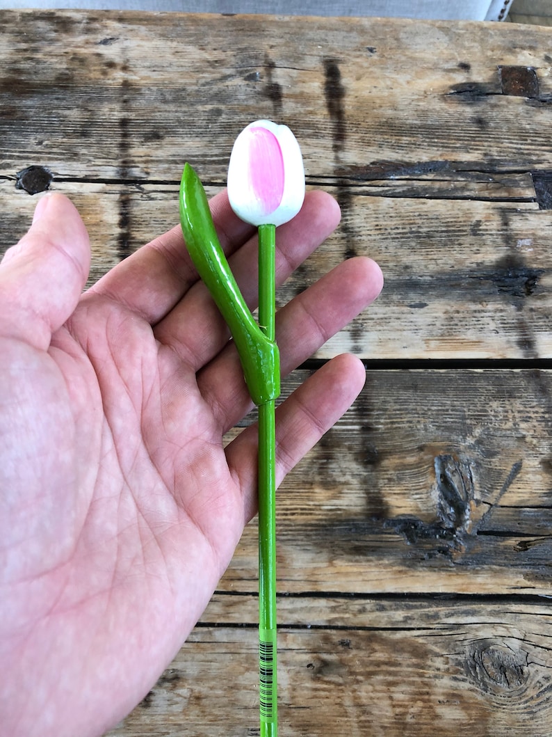 May include: A wooden tulip with a pink and white flower and green stem and leaf.