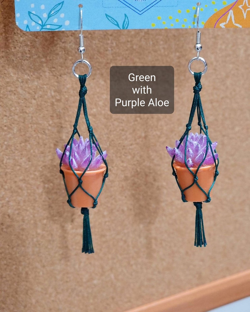 Puede incluir: Un par de pendientes de macram&eacute; verde con una planta suculenta morada en una maceta peque&ntilde;a de terracota. Los pendientes est&aacute;n etiquetados como "Verde con Aloe morado".