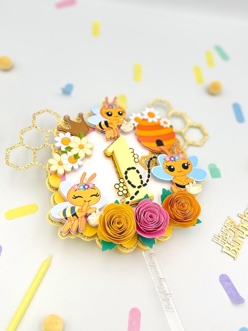 Puede incluir: Adorno para tarta con tem&aacute;tica de abejas. El adorno presenta un n&uacute;mero uno amarillo, abejas de dibujos animados, flores de papel y formas de panal. El adorno est&aacute; decorado con purpurina dorada y est&aacute; dise&ntilde;ado para un primer cumplea&ntilde;os.