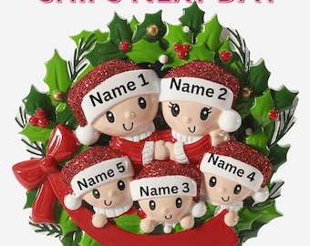 May include: A Christmas ornament featuring a family of five, each wearing a Santa hat with a name label. The ornament is surrounded by a green holly wreath with red berries and a red ribbon. The text "SHIPS NEXT DAY" is at the top.
