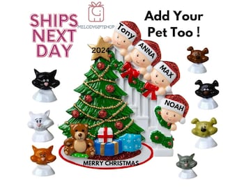 May include: A white ceramic Christmas ornament featuring a family of four peeking around a Christmas tree. The ornament includes the names Tony, Anna, Max, and Noah. The ornament also includes a small teddy bear, a gift box, and a star on top of the tree. The ornament is decorated with red and green accents. The text "Ships Next Day" and "MelodyGiftshop" are visible in the top left corner of the image. The text "Add Your Pet Too!" is visible in the top right corner of the image. The text "Merry Christmas" is visible at the bottom of the ornament.