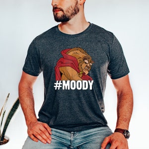 May include: A dark gray t-shirt with a cartoon image of the Beast from Beauty and the Beast. The Beast is wearing a red cape and has a grumpy expression. The text "#MOODY" is printed below the image.