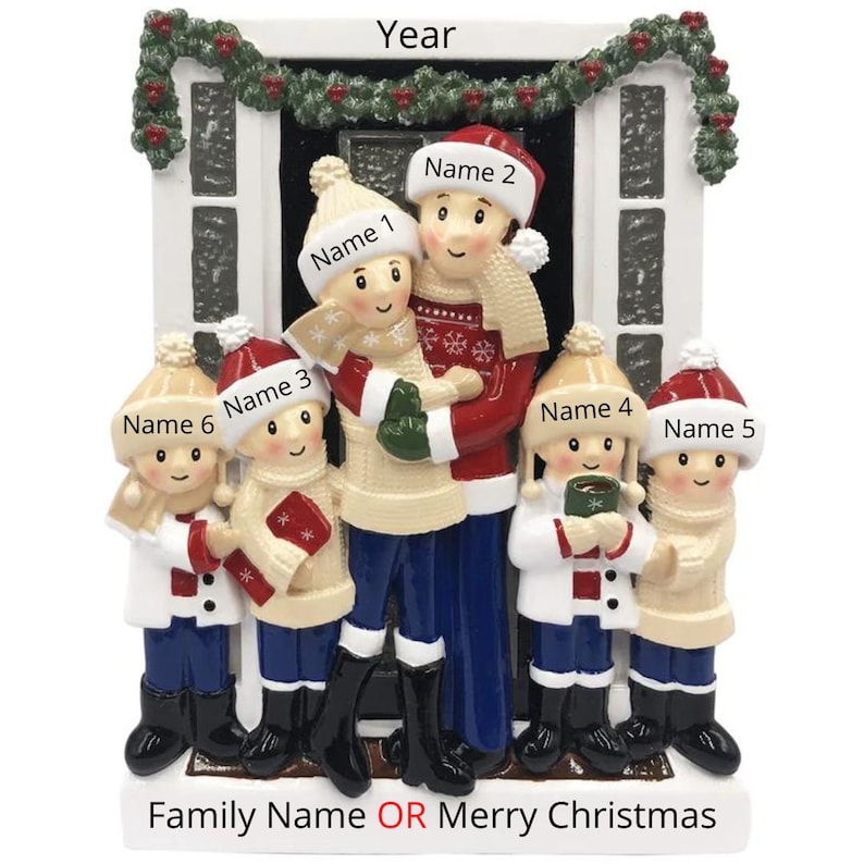 May include: A white and red Christmas ornament featuring a family of six standing in front of a house. The ornament is decorated with a red and white wreath, a red door, and a white snow-covered roof. The family is dressed in winter clothes and is holding gifts and mugs. The text "Family Name OR Merry Christmas" is printed on the bottom of the ornament.