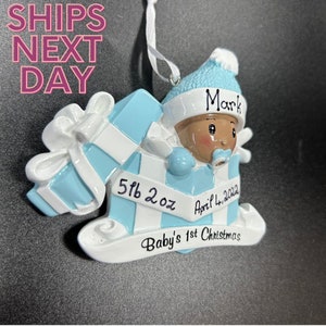 Op de afbeelding: Blauw en wit baby's eerste kerst ornament met een babyjongen die een blauwe muts en een speen draagt. De ornament heeft de tekst "Mark", "5 lb 2 oz", "April 4, 2022", en "Baby's 1st Christmas".