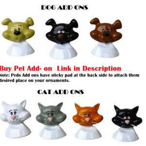 May include: A set of colorful, cartoon-style dog and cat ornaments. The ornaments are made of plastic and have a sticky pad on the back for attaching to surfaces. The text "DOG ADD ONS" and "CAT ADD ONS" is displayed above the ornaments.