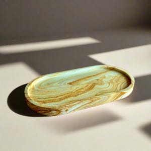 May include: An oval-shaped tray with a marbled design in shades of blue, brown, and white. The tray is made of resin and has a smooth, glossy finish.