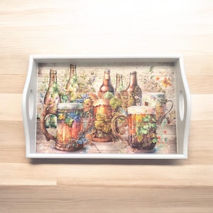May include: A white serving tray with a watercolour design featuring beer bottles, mugs, and foliage. The tray has a rectangular shape with rounded corners and integrated handles. The background has a wood grain pattern.