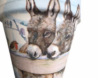 May include: A ceramic planter with a winter scene featuring two donkeys peeking over a fence. The planter has a blue and white background with a robin perched on a branch.