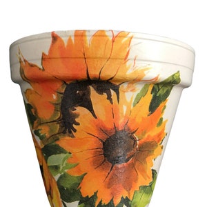 May include: A white terracotta flower pot with a painted design of sunflowers in shades of orange, yellow, and green.