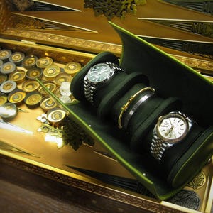 May include: A backgammon set with a gold playing surface and a green watch and jewellery holder. Two watches and two bracelets are displayed. The backgammon board has gold and silver game pieces.