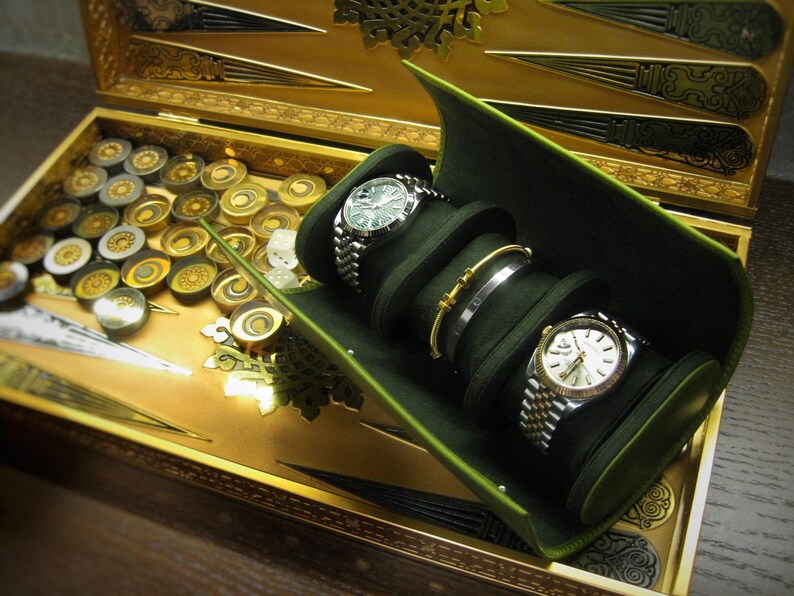 May include: A backgammon set with a gold playing surface and a green watch and jewellery holder. Two watches and two bracelets are displayed. The backgammon board has gold and silver game pieces.
