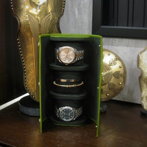 May include: A green and black watch and jewellery travel case with three watch holders and one bracelet holder. Two watches with silver and gold bands and a gold bracelet are visible. The case is open, revealing the contents.