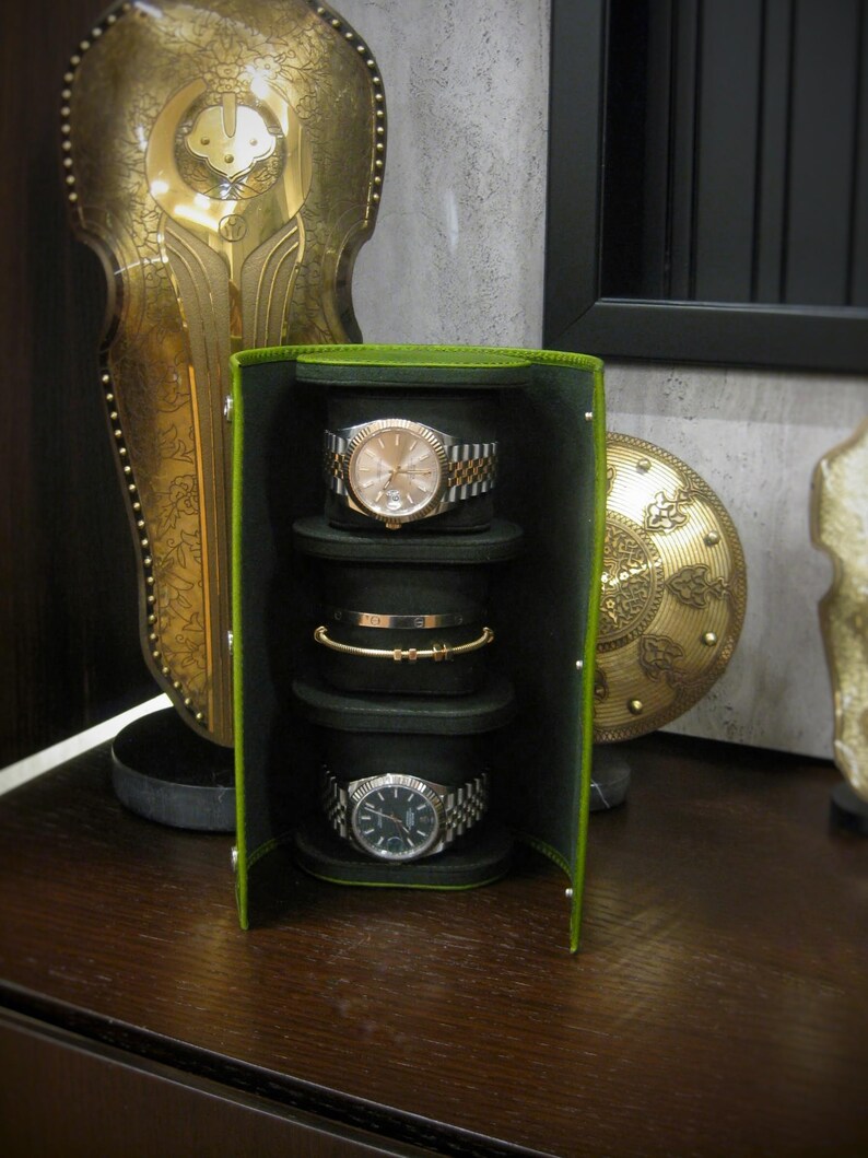 May include: A green and black watch and jewellery travel case with three watch holders and one bracelet holder. Two watches with silver and gold bands and a gold bracelet are visible. The case is open, revealing the contents.