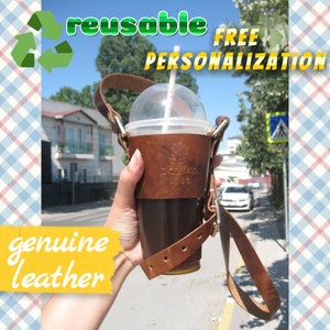 Può includere: Un porta bicchiere in pelle marrone con un cinturino per trasportare una bevanda fredda. Il porta bicchiere ha il testo "ZODVAK 1980" in rilievo. Il porta bicchiere è riutilizzabile ed è fatto di vera pelle.