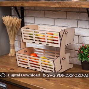 May include: Two-tiered wooden fruit basket with a natural wood finish. The basket is filled with oranges, apples, and other fruits. The basket is on a wooden countertop.