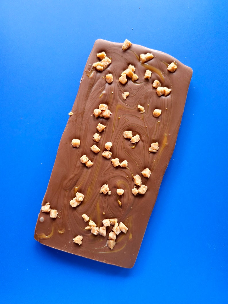 May include: A chocolate bar with a swirl of caramel and pieces of toffee on top.