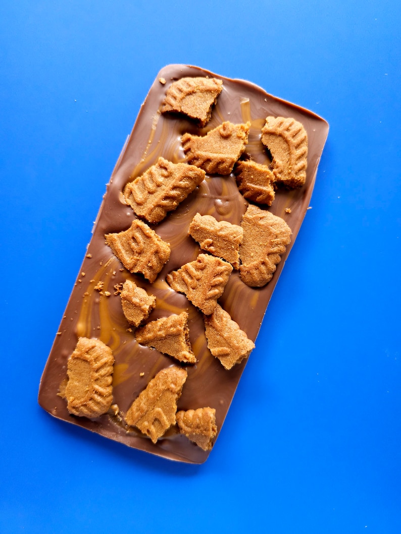 May include: A chocolate bar with broken pieces of shortbread cookies on top. The chocolate is a light brown color and the cookies are a golden brown color. The bar is on a blue background.