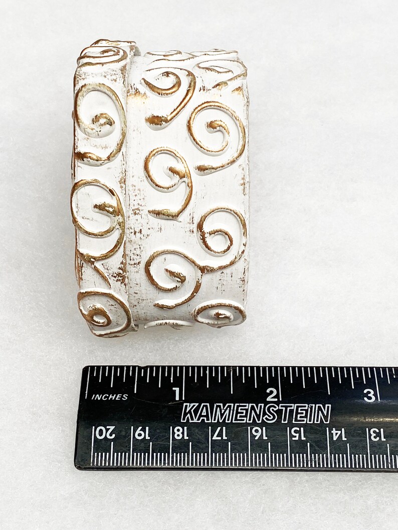May include: White ceramic cylinder with a gold swirl design. The cylinder is approximately 2 inches in diameter.