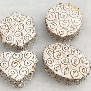 May include: Four white ceramic boxes with a gold swirl design. The boxes are in different shapes, including a heart, a circle, an oval, and a star.