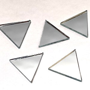 May include: Five small, triangular mirror tiles with reflective surfaces. Each tile has a silver frame and a smooth, mirrored finish. The triangles are arranged on a white surface, showcasing their geometric shape and reflective quality.
