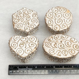 May include: Four white ceramic boxes with gold swirl designs. The boxes are in the shapes of a heart, oval, circle, and hexagon.