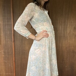 May include: A long-sleeved, knee-length dress with a floral print in shades of pink, blue, and green. The dress has a button-up front and a gathered skirt.