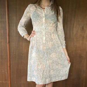 May include: A long-sleeved dress with a floral print in shades of pink, blue, and white. The dress has a button-up front and a fitted waist.