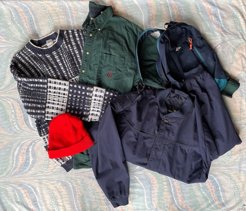 May include: A collection of clothing items including a blue and white striped sweater, a green button-down shirt, a navy blue jacket, and a blue and green backpack.