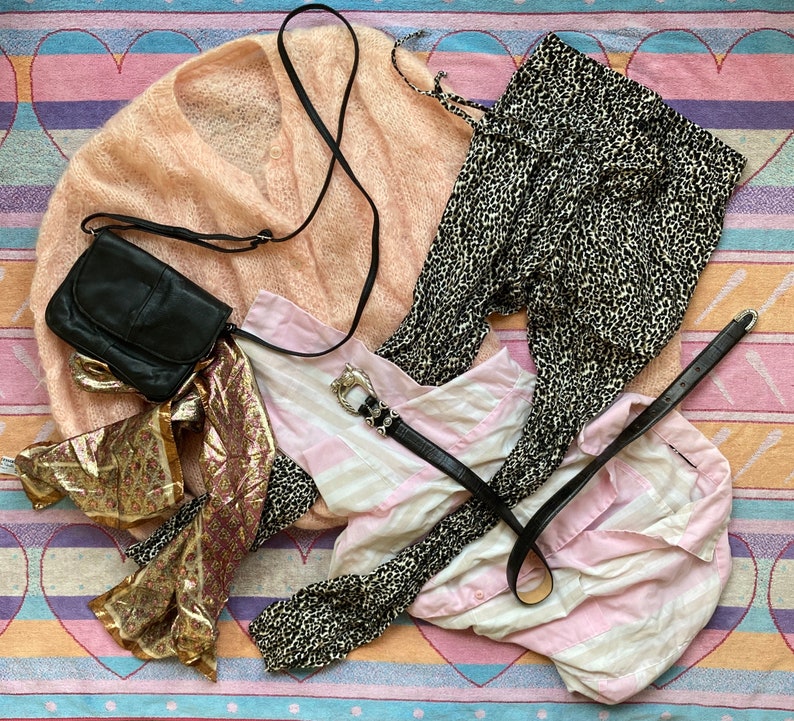 May include: A pink fuzzy cardigan, a black and white animal print skirt, a pink and white striped shirt, a black leather purse with a strap, and a gold and brown scarf.