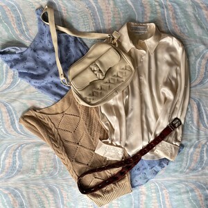 May include: A white satin blouse with a light blue floral print top and a brown leather belt. A white woven bag with a braided strap is on top of the blouse.