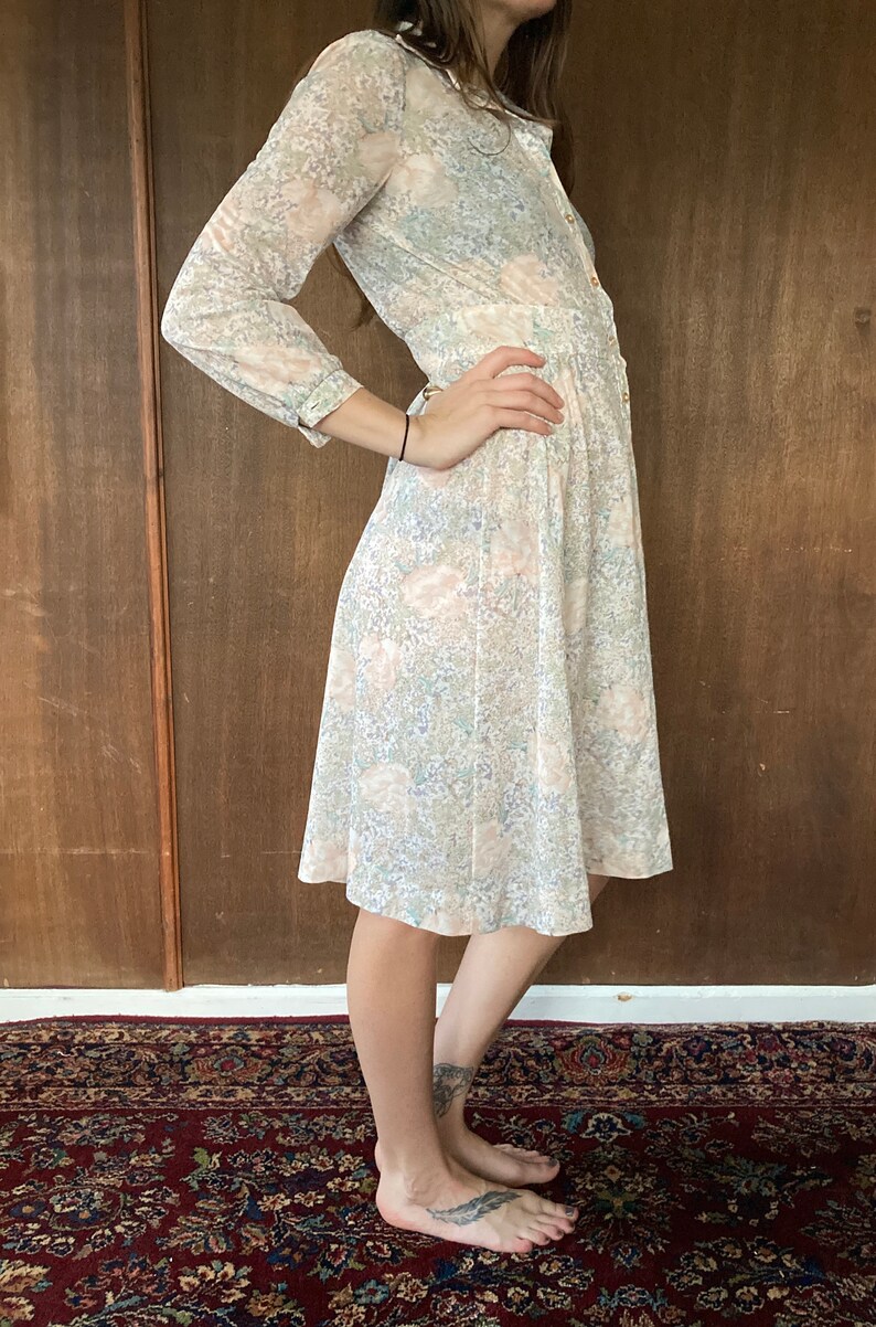 May include: A long-sleeved, knee-length dress with a floral print in shades of pink, blue, and green. The dress has a button-up front and a gathered skirt.