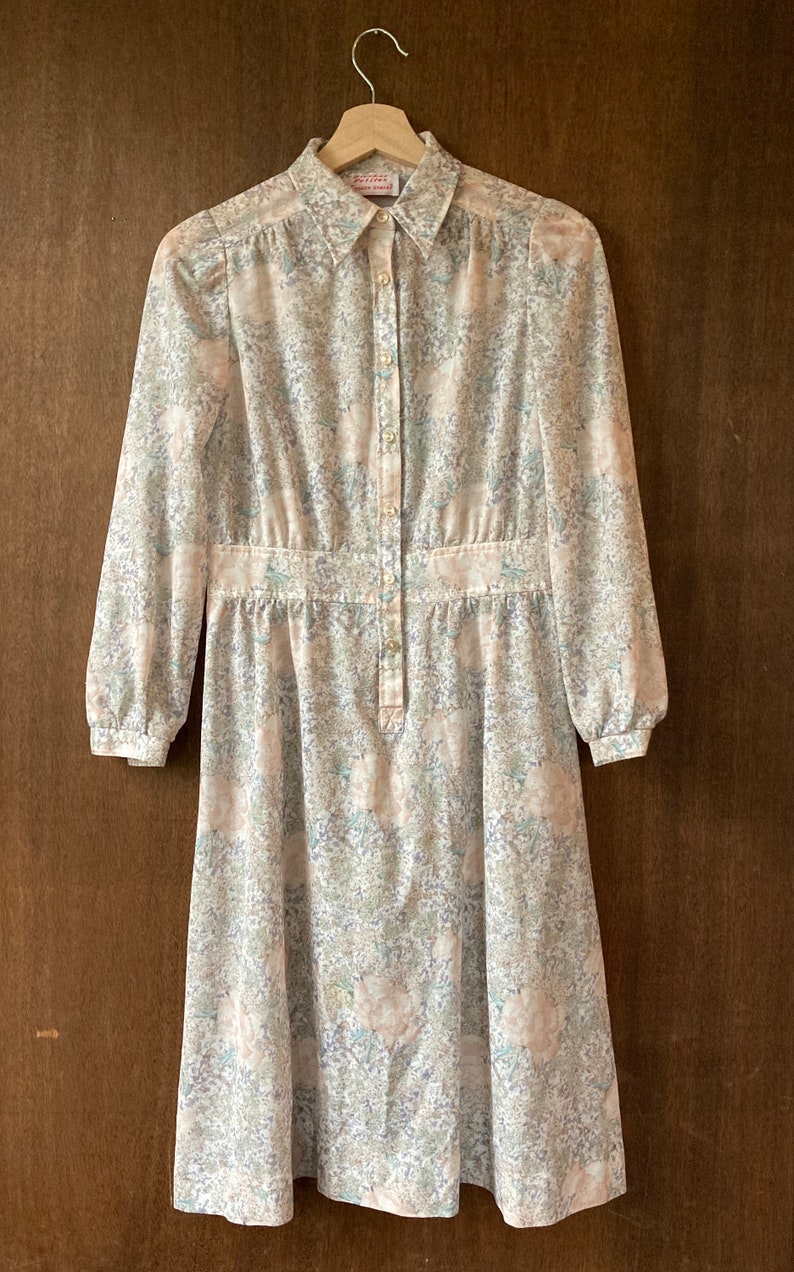 May include: A long-sleeved, button-up dress with a floral print in shades of pink, green, and blue. The dress has a fitted bodice and a flowing skirt.