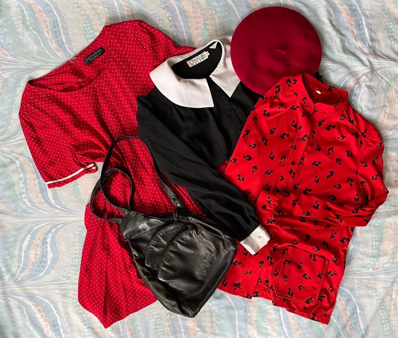 May include: A red polka dot dress, a black dress with a white collar, a red floral print shirt, and a black leather backpack. A red beret is also included.