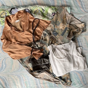 May include: A collection of clothing items including a brown satin blouse, a white tank top, and a patterned dress with a brown leather purse.