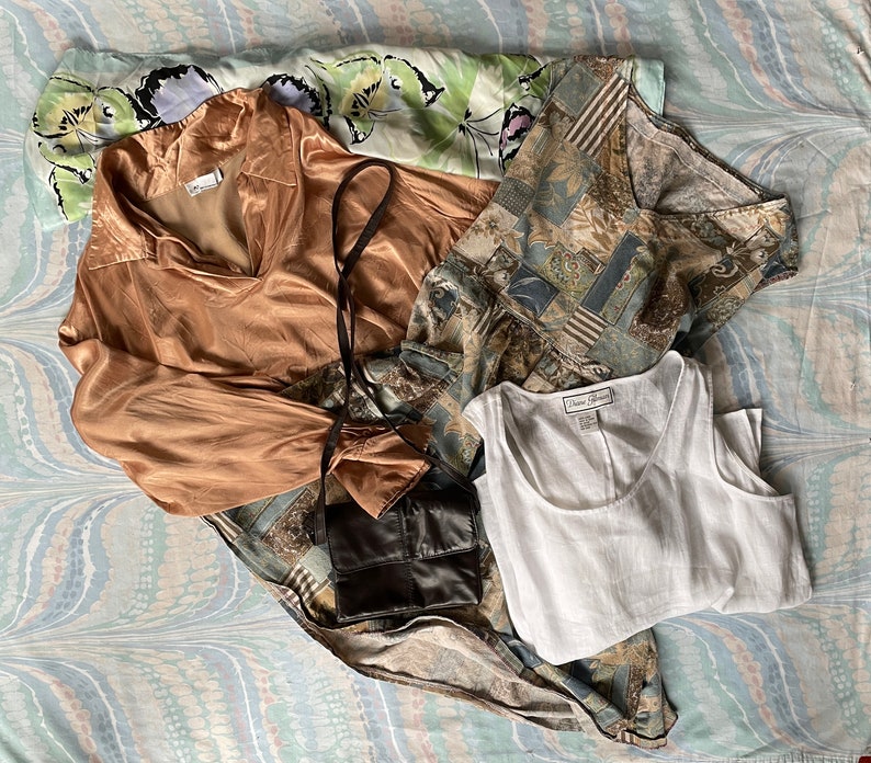 May include: A collection of clothing items including a brown satin blouse, a white tank top, and a patterned dress with a brown leather purse.