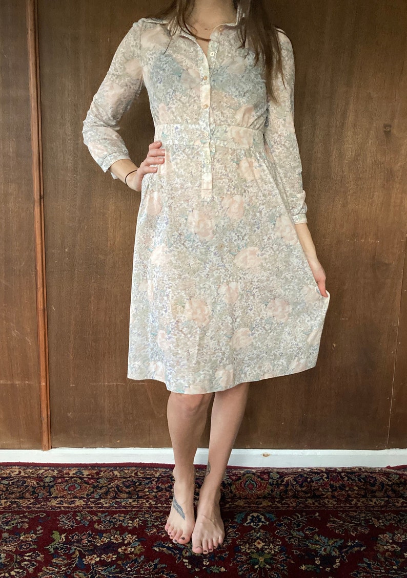 May include: A long-sleeved dress with a floral print in shades of pink, blue, and white. The dress has a button-up front and a fitted waist.