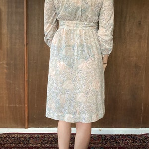 May include: A long-sleeved dress with a floral print in shades of pink, white, and blue. The dress has a collared neckline, a belt at the waist, and a knee-length skirt.