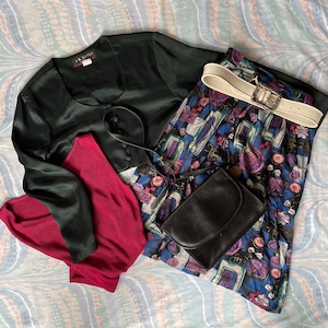 May include: A black satin top with a red and black striped undershirt, a black and white patterned skirt, and a white belt with a silver buckle.