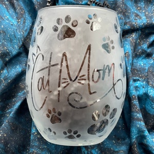 May include: A frosted glass wine glass with the text "Cat Mom" and paw prints etched into the surface.