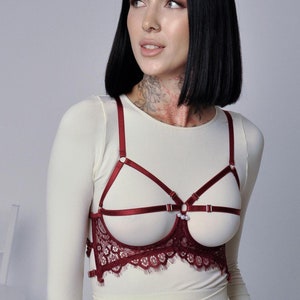 May include: A red lace lingerie top with adjustable straps and a delicate pearl accent. The top features a criss-cross design and a scalloped lace trim.
