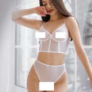 Op de afbeelding: Witte lingerie set met een doorschijnend mesh topje en bijpassende broek. Het topje heeft een gecorseteerd lijfje en verstelbare bandjes. De broek heeft een hoge taille.