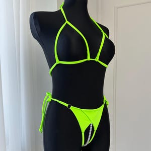 Op de afbeelding: Neon groene bikiniset op een zwarte mannequin. De bikinitop heeft een halternekontwerp en de broek heeft een veter en een pareldetail. De badkleding is gemaakt van een heldere, opvallende stof.