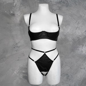 May include: Black lingerie set with a satin bra and matching panty. The bra has a plunging neckline and the panty has a criss-cross strap design.