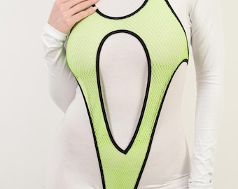 Op de afbeelding: Een witte bodysuit met lange mouwen en een neon groen mesh overlay met zwarte rand. De overlay heeft een uniek uitgesneden ontwerp.