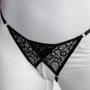 May include: Black lace underwear with a delicate floral pattern and a string design. A string of pearls is visible in the center. The lingerie features a minimalist design with metal ring accents.